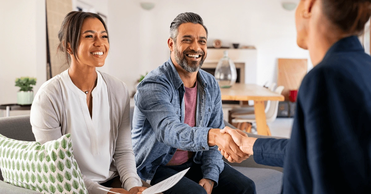 Probate Real Estate Specialist shaking hands with couple in living room. Kid Breuklen Realty Group