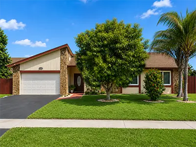 Front view of 8330 NW 54th St Lauderhill FL with 2-car garage, green lawn, fruit tree, and palm tree.
