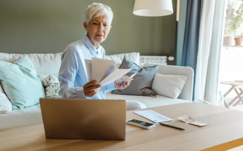 Reading bill on sofa with computer open in 33009